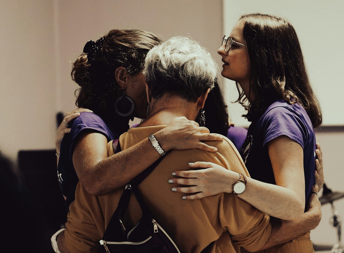 Three volunteers in matching shirts holding one another in a group embrace